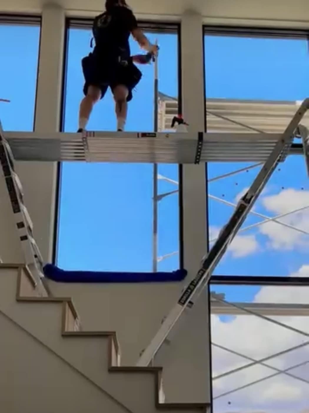 Imperial crew member on a ladder platform cleaning tall atrium windows from inside