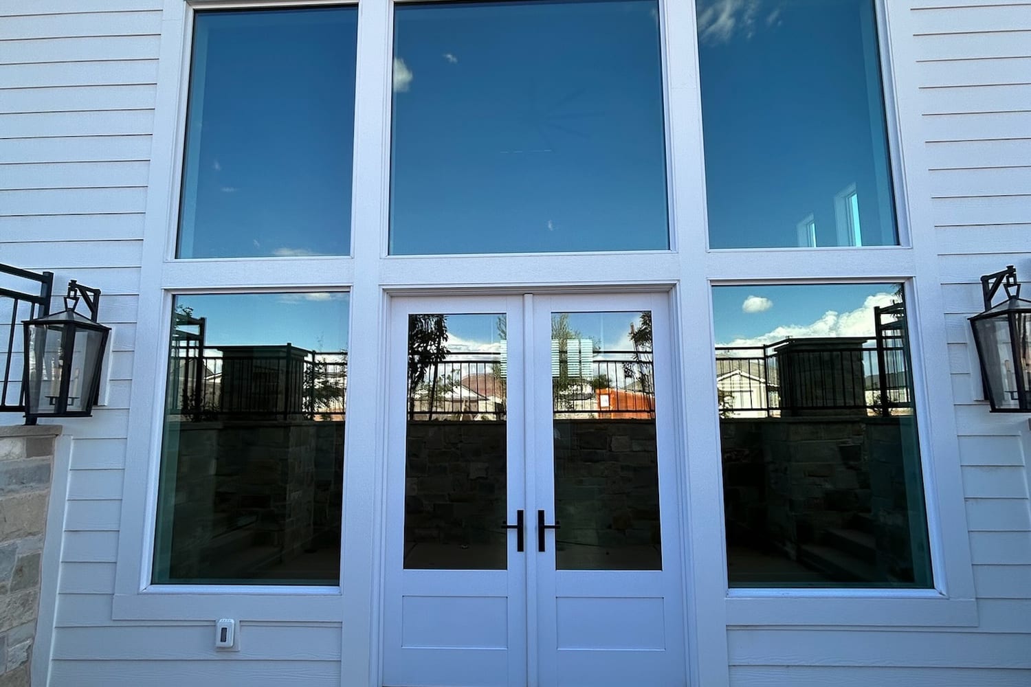 French doors and transom glass with film, reflecting sky and stonework from outside