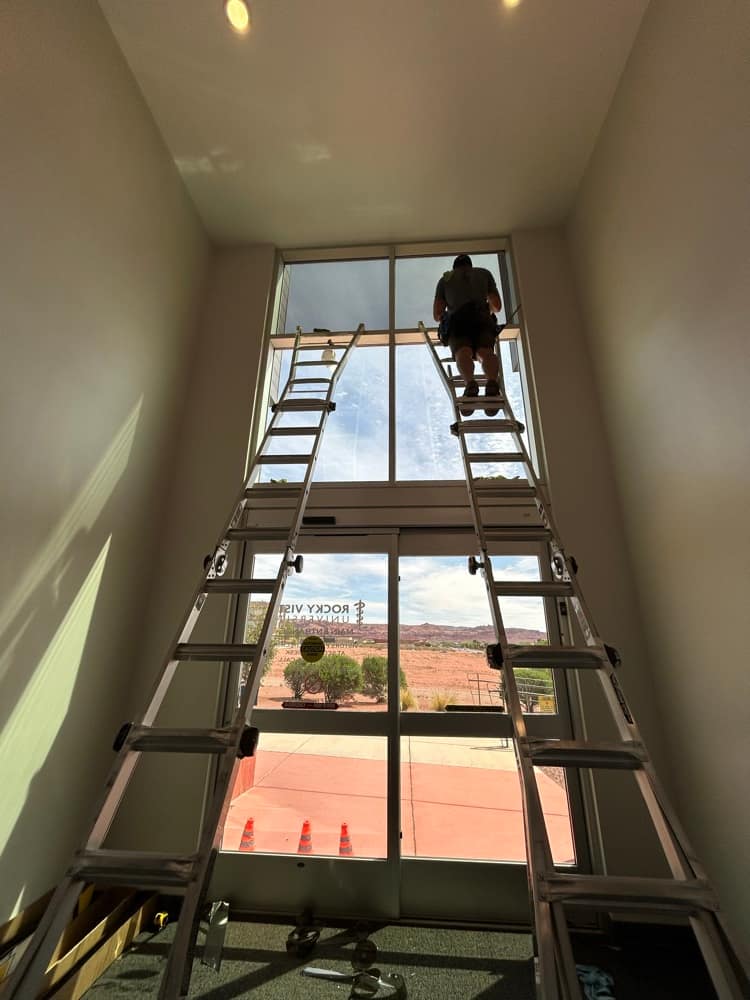Imperial crew member on a tall ladder cleaning two-story atrium windows