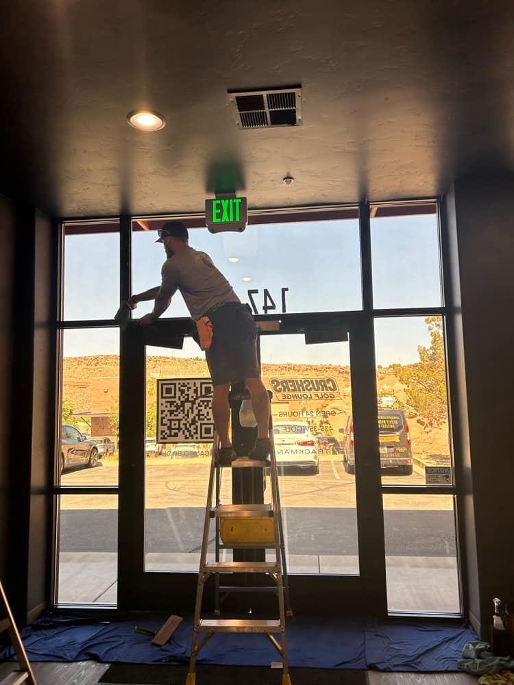 Crew member on a ladder servicing commercial storefront glass with red rock behind